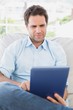 Focused man sitting on the couch using his tablet Focused man sitting on the couch using his tablet