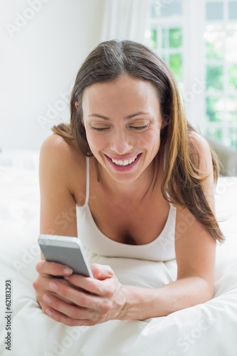 Photo: Smiling woman text messaging in bed Smiling woman text messaging in bed