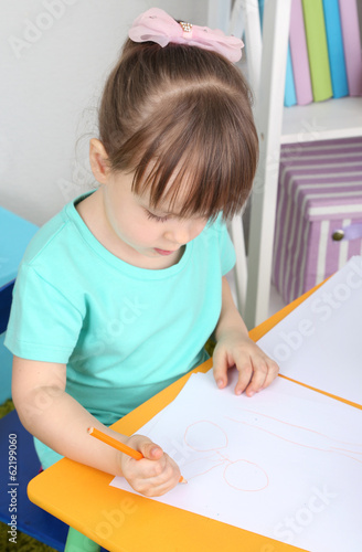 Photo: Little girl draws sitting at table in room Little girl draws sitting at table in room
