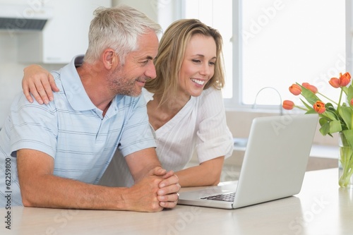 Photo: Cheerful couple using laptop together at the worktop Cheerful couple using laptop together at the worktop