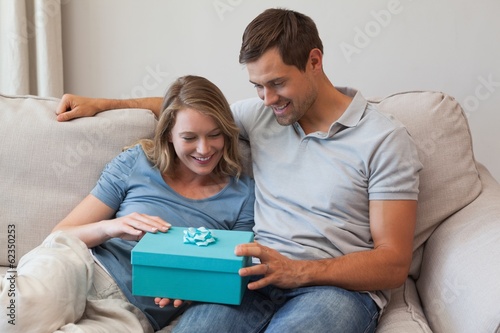 Photo: Woman receiving a gift by man in living room Woman receiving a gift by man in living room