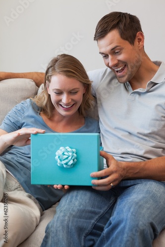 Photo: Happy woman receiving a gift by man in living room Happy woman receiving a gift by man in living room