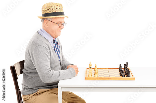 Photo: Man sitting at table and looking at a chessboard Man sitting at table and looking at a chessboard