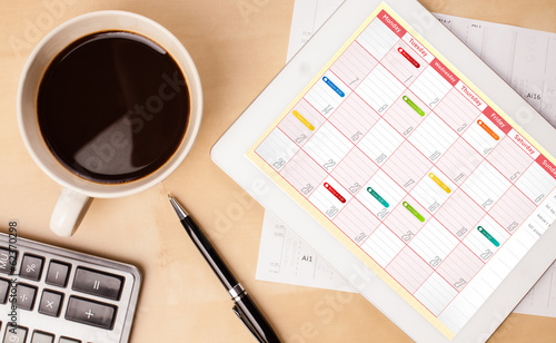 Photo: Tablet pc showing calendar on screen with a cup of coffee on a d Tablet pc showing calendar on screen with a cup of coffee on a d