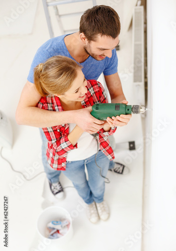 Photo: smiling couple drilling hole in wall at home smiling couple drilling hole in wall at home