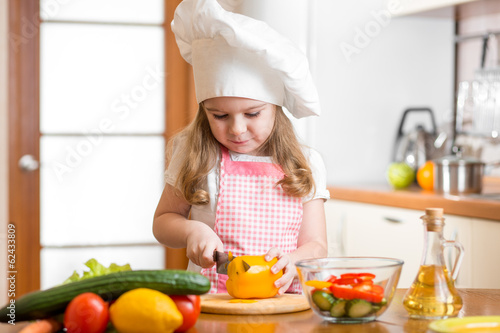 Photo: Kid girl weared as cook cutting vegetables Kid girl weared as cook cutting vegetables