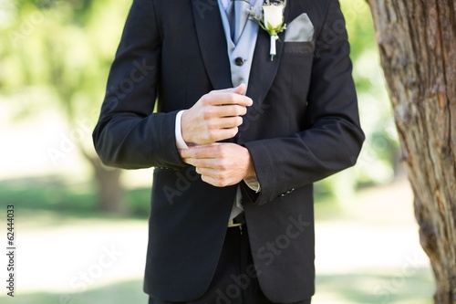 Photo: Groom adjusting sleeve in garden Groom adjusting sleeve in garden