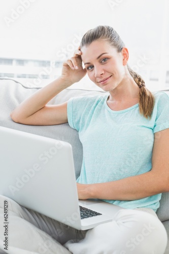 Photo: Smiling woman sitting on couch using her laptop Smiling woman sitting on couch using her laptop