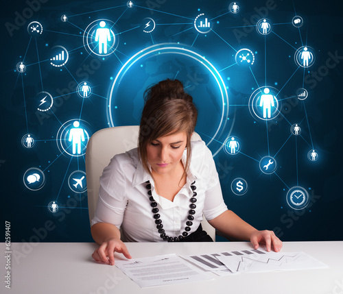 Photo: Businesswoman sitting at desk with social network icons Businesswoman sitting at desk with social network icons