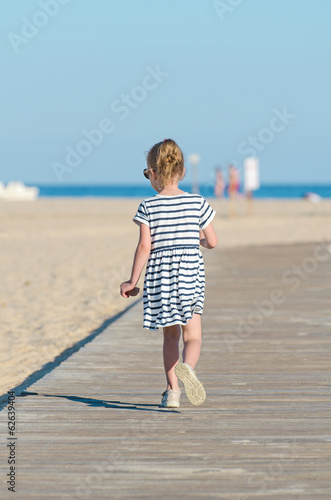 Photo: Little girl on beach vacation. From the back. Little girl on beach vacation. From the back.