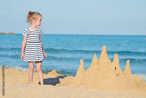 Photo: Little girl with sand castle on the beach. Little girl with sand castle on the beach.