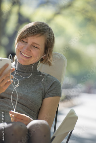 Foto: City Life. A Woman Sitting In A Camping Chair In The Park, Listening To Music Wearing Headphones. City Life. A Woman Sitting In A Camping Chair In The Park, Listening To Music Wearing Headphones.