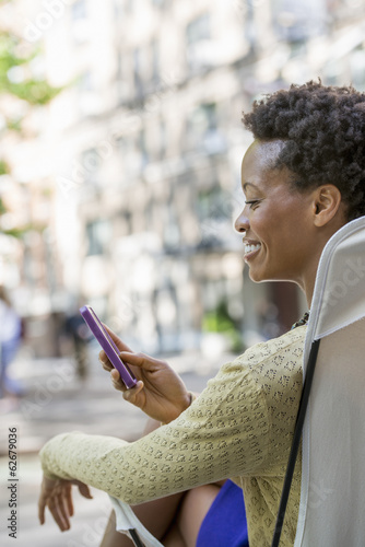 Foto: City Life. A Woman Sitting In A Camping Chair In A City Park, Checking Her Cell Phone. City Life. A Woman Sitting In A Camping Chair In A City Park, Checking Her Cell Phone.