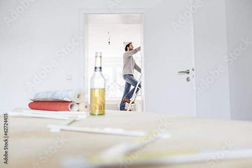 Photo: Mann steht auf Stufenleiter, Tapeten und Bierflasche im Vordergrund Mann steht auf Stufenleiter, Tapeten und Bierflasche im Vordergrund