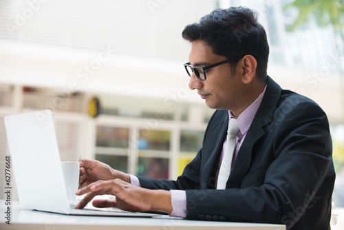 Photo: young indian business man on laptop and coffee at a cafe young indian business man on laptop and coffee at a cafe