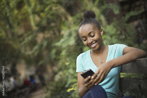 Foto: Scenes from urban life in New York City. A young teenage girl sitting on a bench, looking at a pad screen or texting. Scenes from urban life in New York City. A young teenage girl sitting on a bench, looking at a pad screen or texting.
