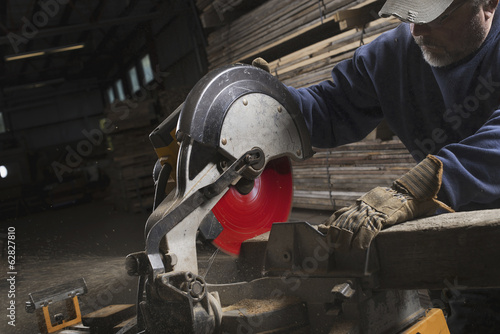 Foto: A reclaimed lumber workshop. A man in protective eye goggles using a circular saw to cut timber. A reclaimed lumber workshop. A man in protective eye goggles using a circular saw to cut timber.