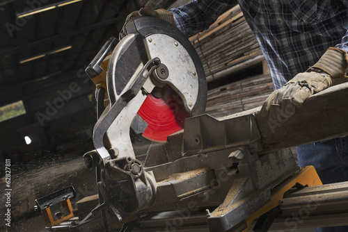 Foto: A reclaimed lumber workshop. A man in protective eye goggles using a circular saw to cut timber. A reclaimed lumber workshop. A man in protective eye goggles using a circular saw to cut timber.