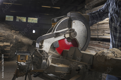 Foto: A reclaimed lumber workshop. A man in protective eye goggles using a circular saw to cut timber. A reclaimed lumber workshop. A man in protective eye goggles using a circular saw to cut timber.
