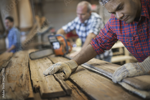 Foto: A reclaimed lumber workshop. A group of people working. A man measuring and checking planks of wood for re-use and recycling. A reclaimed lumber workshop. A group of people working. A man measuring and checking planks of wood for re-use and recycling.