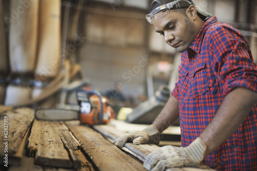 Foto: A reclaimed lumber workshop. A man measuring and checking planks of wood for re-use and recycling. A reclaimed lumber workshop. A man measuring and checking planks of wood for re-use and recycling.