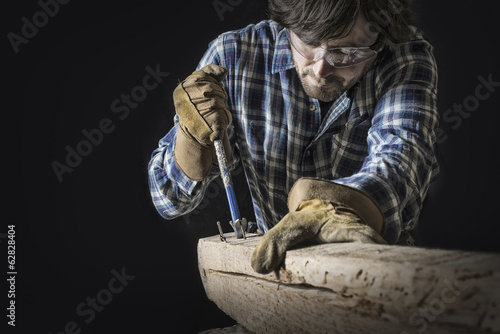 Foto: A man working in a reclaimed lumber yard workshop. Holding tools and extracting nails from a knotted and uneven piece of wood. A man working in a reclaimed lumber yard workshop. Holding tools and extracting nails from a knotted and uneven piece of wood.