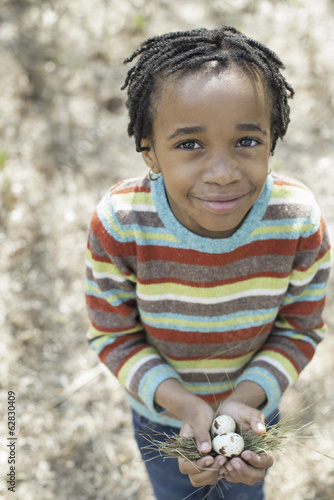 Foto: A New York city park in the spring. A small boy in a striped shirt, holding a nest with three birds eggs. A New York city park in the spring. A small boy in a striped shirt, holding a nest with three birds eggs.