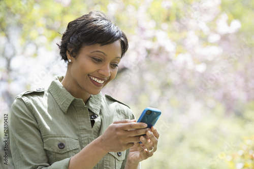 Foto: A New York city park in the spring. Sunshine and cherry blossom. A woman checking her smart phone. A New York city park in the spring. Sunshine and cherry blossom. A woman checking her smart phone.