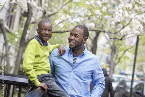 Foto: A New York city park in the spring. Sunshine and cherry blossom. A boy sitting on a fence, beside his father. A New York city park in the spring. Sunshine and cherry blossom. A boy sitting on a fence, beside his father.