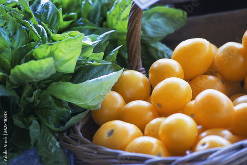 Photo: Organic yellow tomatoes and basil herb leaves on a market stall. Organic yellow tomatoes and basil herb leaves on a market stall.
