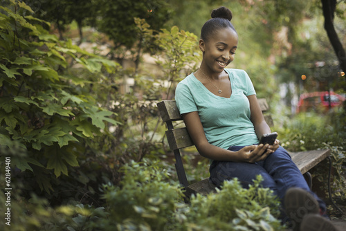 Foto: Scenes from urban life in New York City. A young teenage girl sitting on a bench, looking at a pad screen or texting. Scenes from urban life in New York City. A young teenage girl sitting on a bench, looking at a pad screen or texting.