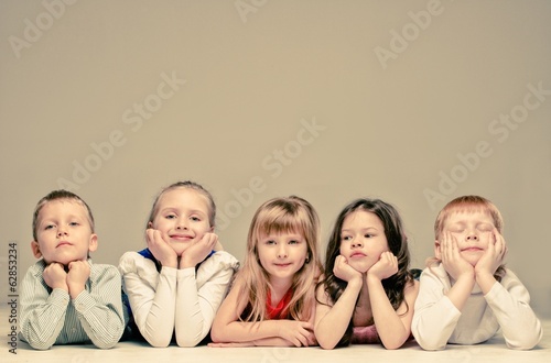 Photo: Group of little children lying in a row isolated on grey Group of little children lying in a row isolated on grey