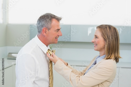 Photo: Woman adjusting businessman's tie in kitchen Woman adjusting businessman's tie in kitchen