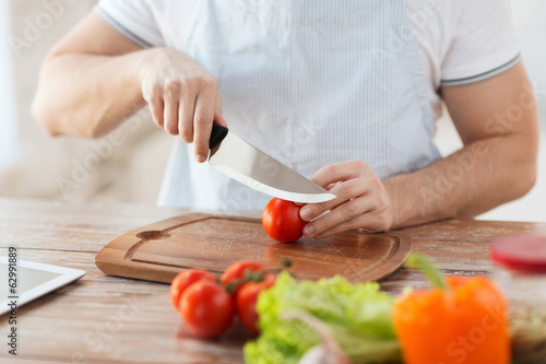 Photo: male hand cutting tomato on board with knife male hand cutting tomato on board with knife
