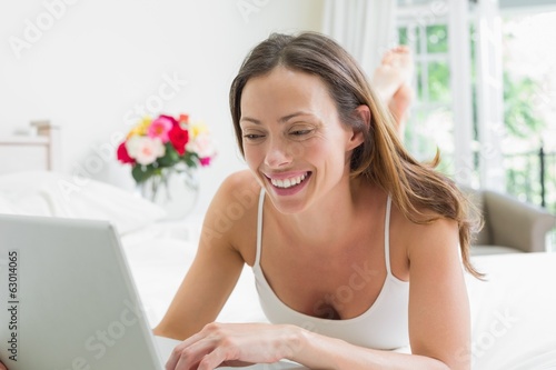 Photo: Smiling relaxed woman using laptop in bed Smiling relaxed woman using laptop in bed