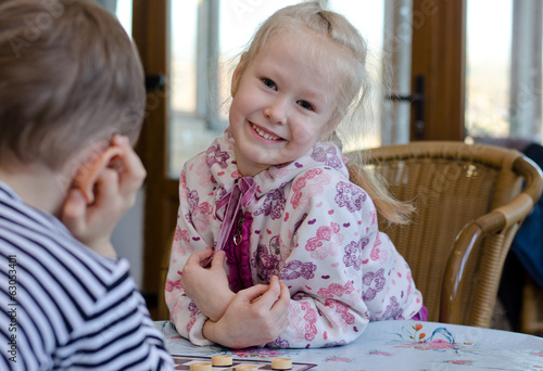 Photo: Beautiful little girl playing a game of checkers Beautiful little girl playing a game of checkers