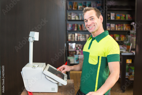 Photo: Cashier at cash register in shop or store Cashier at cash register in shop or store