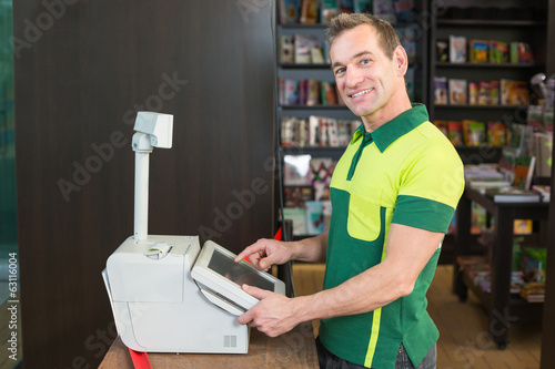 Photo: Cashier at cash register in shop or store Cashier at cash register in shop or store