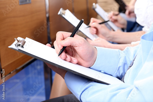 Photo: Hands holding pens and making notes at conference Hands holding pens and making notes at conference