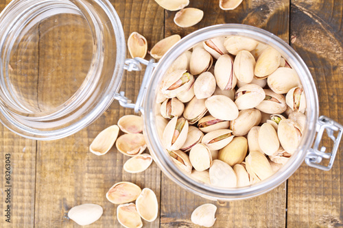 Photo: Pistachio nuts in glass jar on wooden background Pistachio nuts in glass jar on wooden background
