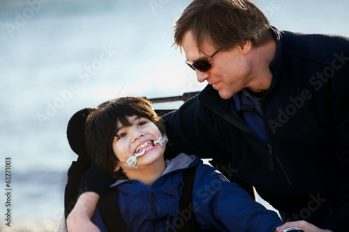 Photo: Father sitting with disabled son along lake shore Father sitting with disabled son along lake shore
