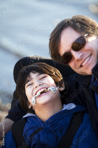 Photo: Father sitting with disabled son along lake shore Father sitting with disabled son along lake shore