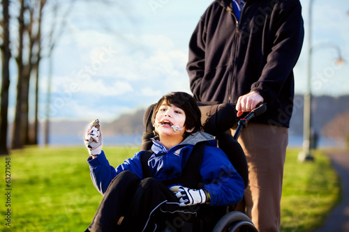 Photo: Father walking with disabled son in wheelchair Father walking with disabled son in wheelchair