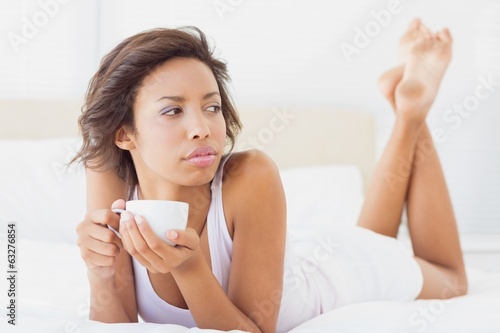 Photo: Pretty brunette lying on bed thinking holding a cup Pretty brunette lying on bed thinking holding a cup