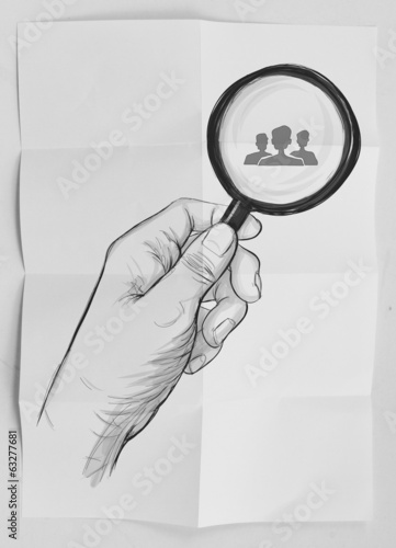 Photo: hand holding magnifier glass looking for employee on crumpled pa hand holding magnifier glass looking for employee on crumpled pa