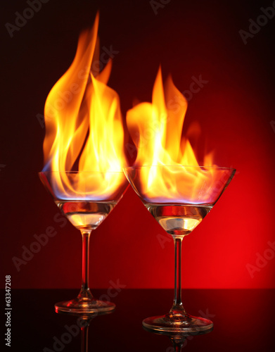 Photo: Glasses with burning alcohol on red background Glasses with burning alcohol on red background
