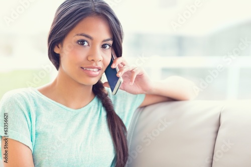 Photo: Smiling girl sitting on sofa making a phone call Smiling girl sitting on sofa making a phone call
