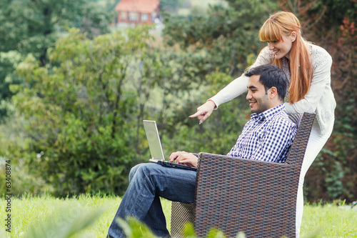 Photo: Couple or friends using laptop, outdoor - outside Couple or friends using laptop, outdoor - outside