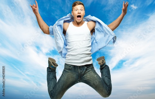 Photo: Funny man in blue shirt and jeans jumping against blue sky Funny man in blue shirt and jeans jumping against blue sky