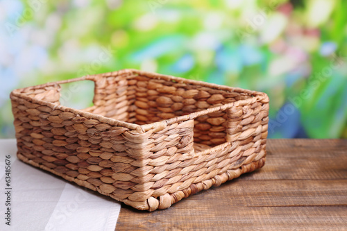 Photo: Empty wicker basket on wooden table, on bright background Empty wicker basket on wooden table, on bright background